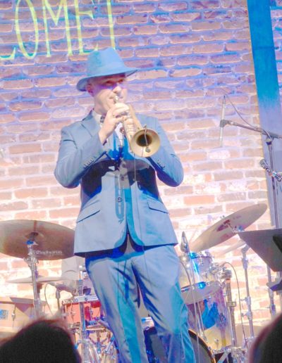 Nicolas sur scène joue de la trompette v^tu d'un costume bleu et d'un chapeau bleu